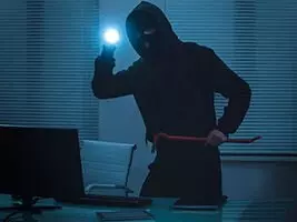 Ein Einbrecher mit Taschenlampe steht vor einem Laptop