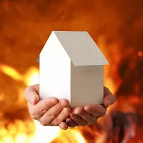 Fit im Ausbau Brandschutz 2 Hände halten ein Modellhaus, brenndener Hintergrund